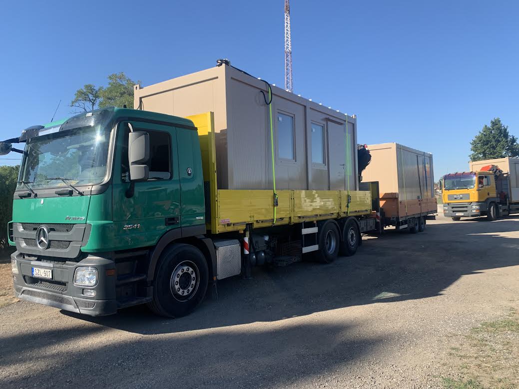 A Talabos Teherfuvar Mercedes-Benz Actros darus teherautója pótkocsival, lakókonténerekkel megrakva, mögötte a sárga MAN darus